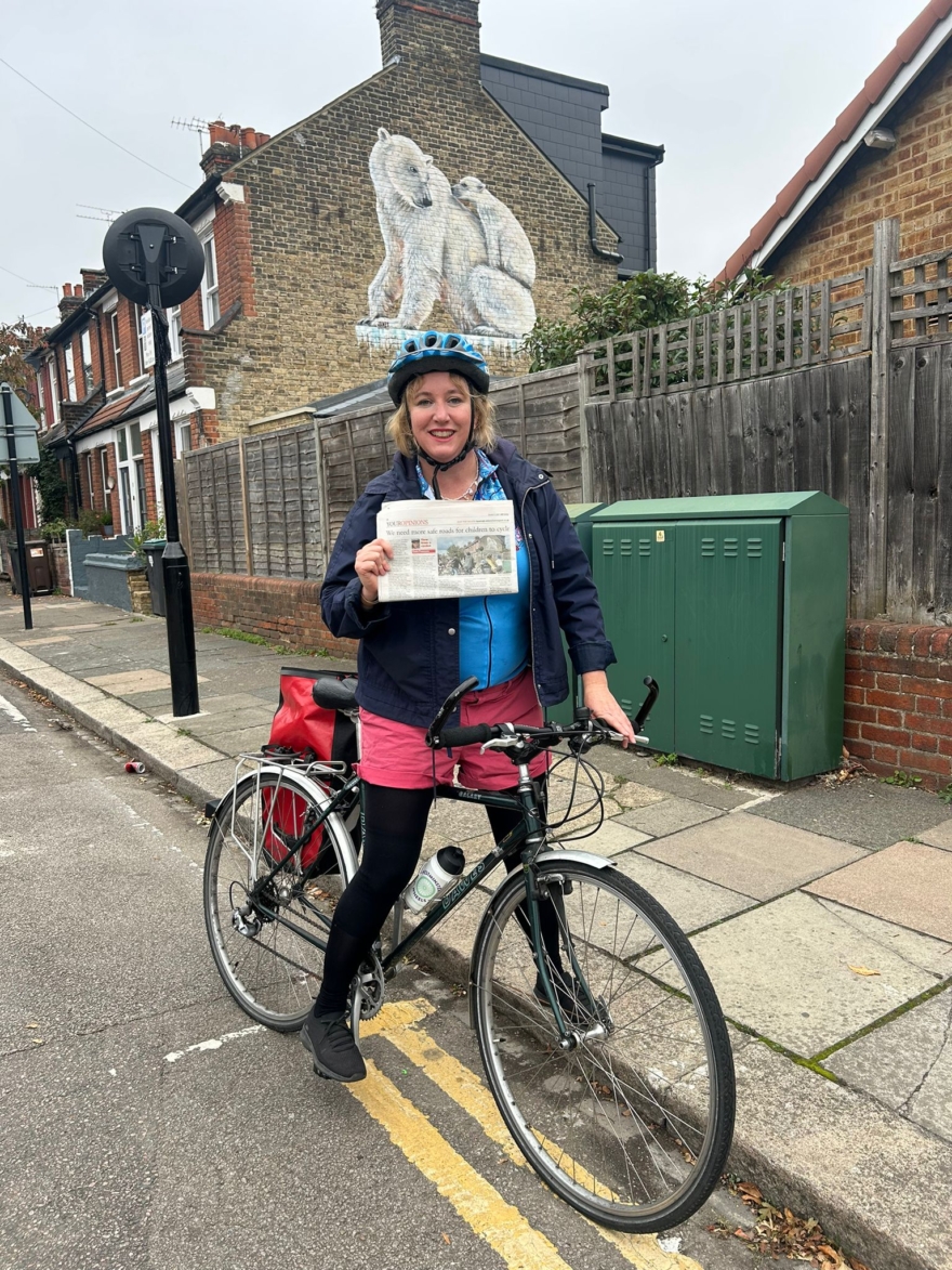 Carla Francome holding her Ham & High article on safer cycling for children in Haringey in front of the polar bears mural by James Straffon